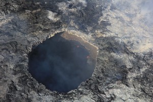 Aug. 4: The pit west of the Puʻu ʻŌʻō crater, shown here, is overhung on most sides and may continue to widen with time. The lava pond inside is relatively placid, appearing as a black surface, usually with a few tiny spattering areas along the edge. USGS/HVO photo.