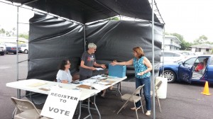 Election worker Sue Irvine, center, accepts a voter registration form today at the Hilo drive-thru location. Photo by Dave Smith.