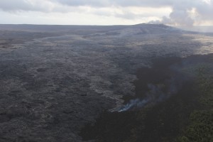 A breakout from the lava tube has also been active on the upper part of the flow field near Puʻu ʻŌʻō since December 5. The smoke is from a narrow finger of lava burning lichen on an older Puʻu ʻŌʻō lava flow. Puʻu ʻŌʻō is at upper right. The view is to the south-southwest. HVO photo.