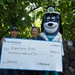 Just before the UnitedHealthcare IRONKIDS Keiki Dip-n-Dash, UnitedHealthcare mascot Dr. Health E. Hound helps present a $3,000 check to Kama‘aina Kids to support its youth health programs. (Left to right: Mark Nishiyama, Vice President of Kama’aina Kids; Dr. Ron Fujimoto, Chief Medical Officer for UnitedHealthcare's Community Plan for Hawaii; Dr. Health E. Hound, UnitedHealthcare). Photo credit: UnitedHealthcare.