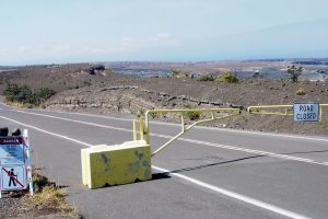 Layers of explosive deposits erupted from Kīlauea Volcano in 17th and 18th centuries are visible in a road cut just beyond the gate at Keanakākoʻi Crater. This section of Crater Rim Drive has been closed since 2008, when the still-erupting vent within Halemaʻumaʻu Crater (middle, far right) first opened. USGS photo.