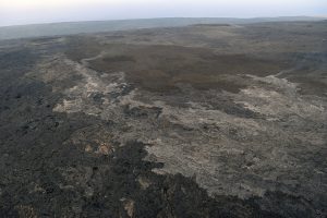 The new lava flow erupting from a vent on the eastern flank of Pu‘u ‘Ō‘ō on Kīlauea Volcano’s East Rift Zone appears silvery compared to older lavas over which it is flowing. The leading edge of the flow (visible fume in the upper left quadrant of photo) was about a mile from Pulama pali (fault scarp) on June 16, 2016. The coastal plain and ocean can be seen beyond the pali at the top of the photo. An HVO webcam (R3cam) provides imagery of this flow. USGS photo.