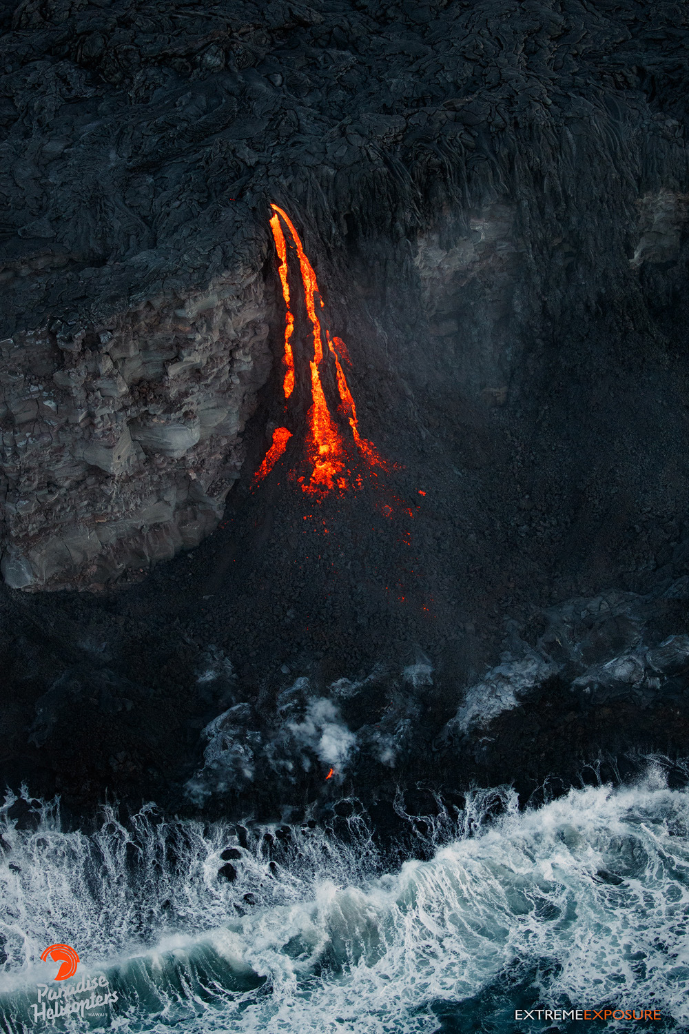 Lava transforms from pahoehoe to ‘a‘a as it cascades down the face of a sea cliff on the Kalapana coastline, building a new delta of land at its base. Paradise Helicopters photo.
