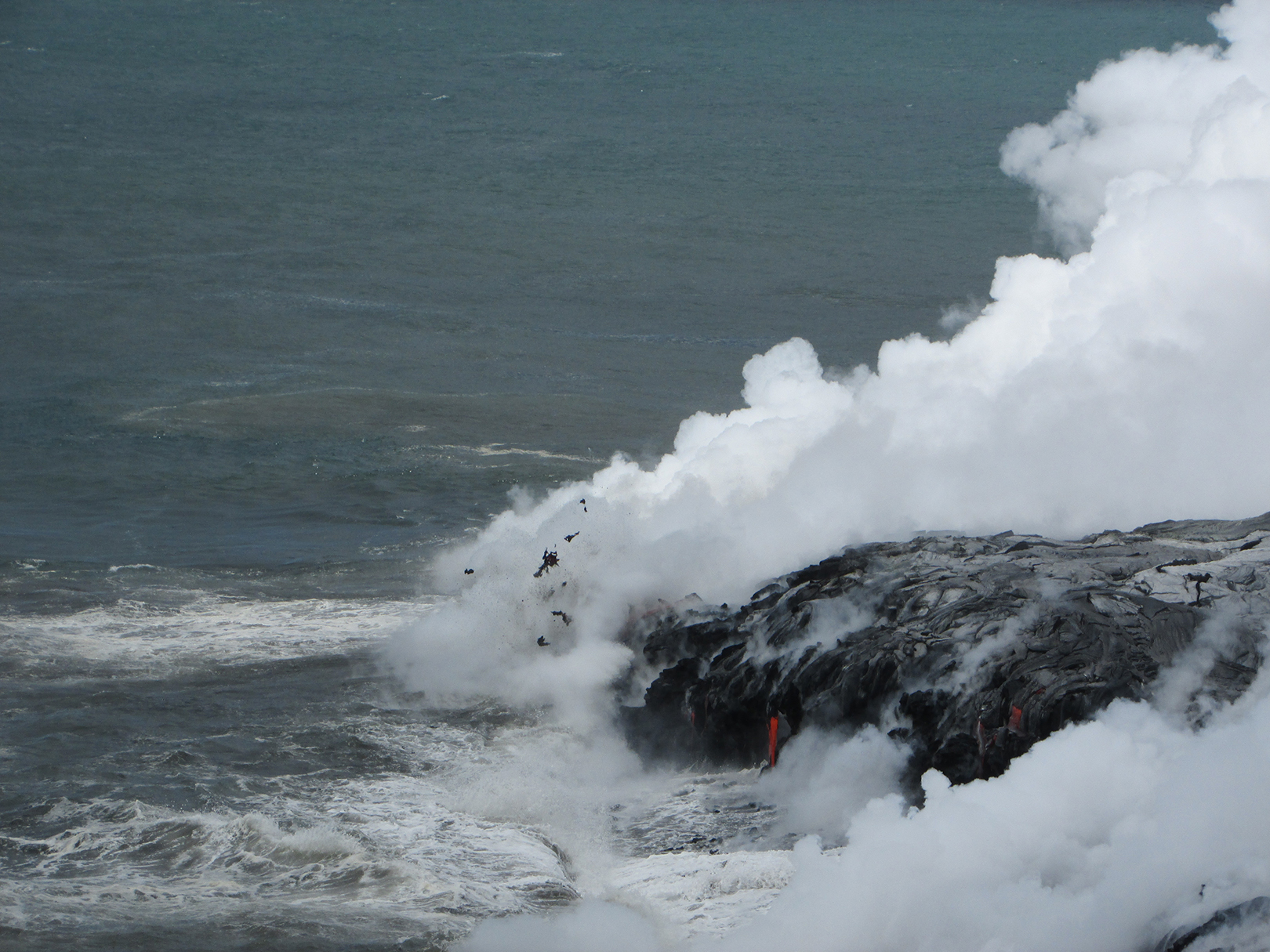 The explosive interaction of hot lava entering cool seawater throws spatter (clots of molten lava, visible at center of image) from the leading edge of the lava delta forming at Kīlauea’s Kamokuna ocean entry. This vigorous interaction also generates a billowy white "laze" plume composed of condensed seawater steam laced with hydrochloric acid and tiny shards of volcanic glass. The plume cloud is especially hazardous for visitors who, in an effort to see the ocean entry, venture beyond posted warning signs along the coast. USGS photo.
