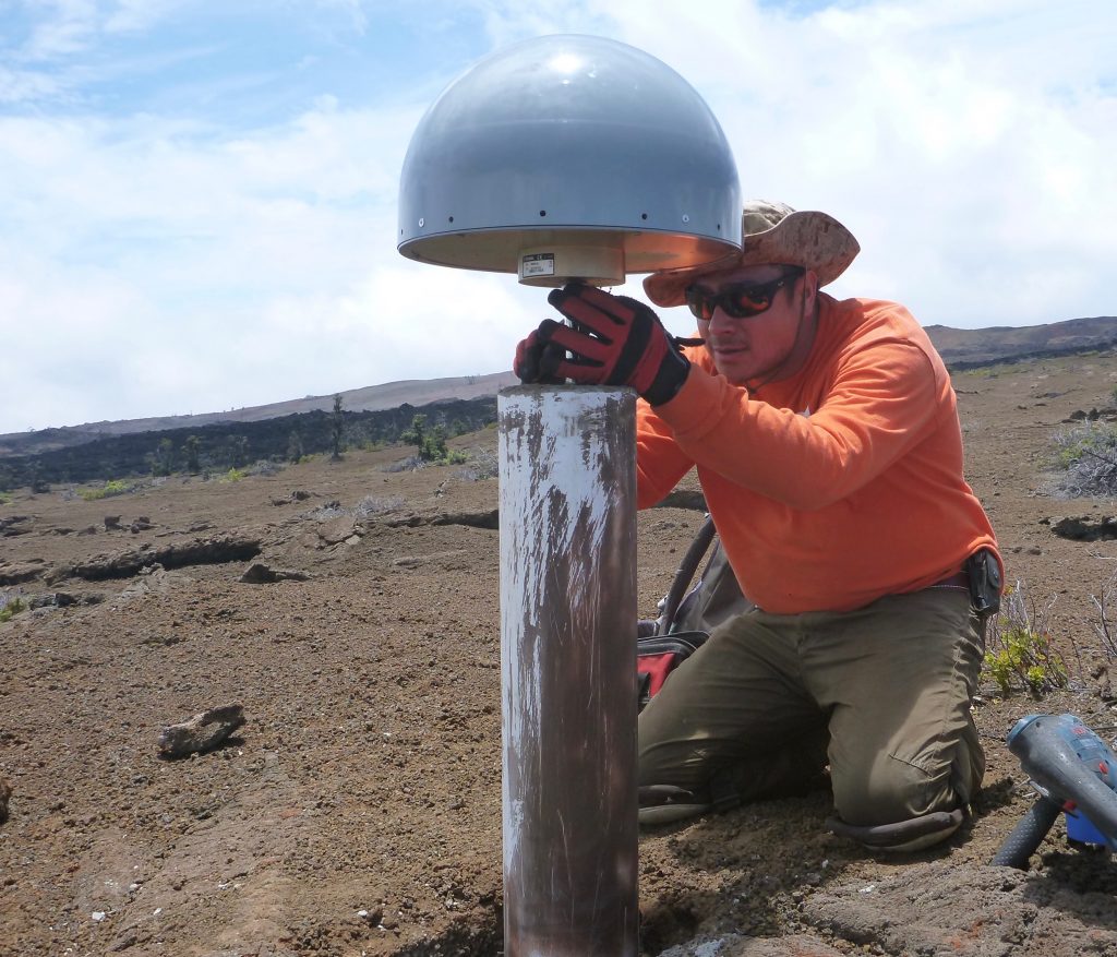 A USGS Hawaiian Volcano Observatory scientist puts the finishing touches on a new permanent GPS station on the slopes on Mauna Loa. The GPS antenna, protected from the elements by the grey radome, is solidly attached to the ground via a cement-reinforced steel rod. GPS is a critical tool for tracking ground motion on Hawaiian volcanoes. USGS photo.